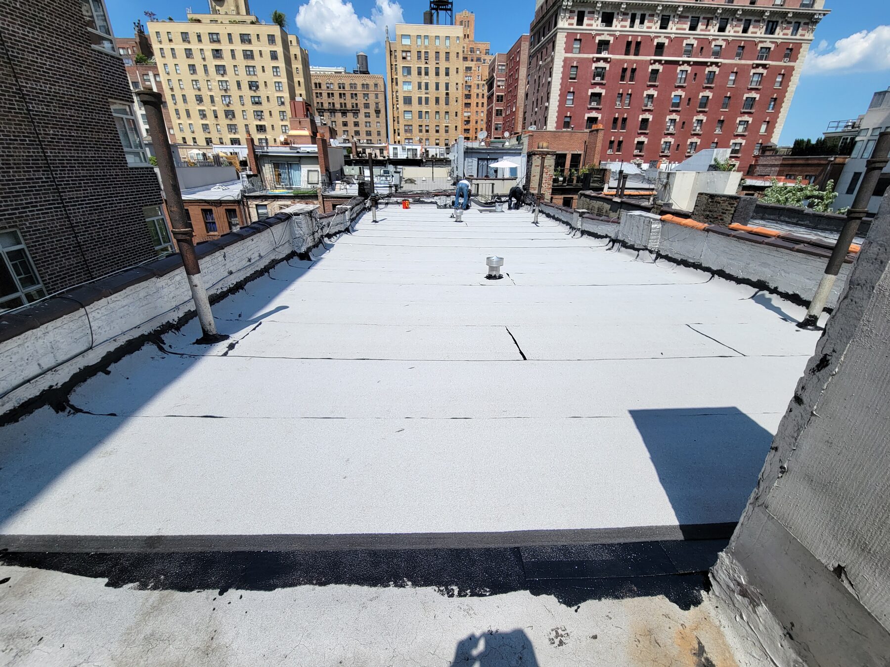 Crew installing new white asphalt roofing membrane during full roof replacement, Upper West Side, Manhattan
